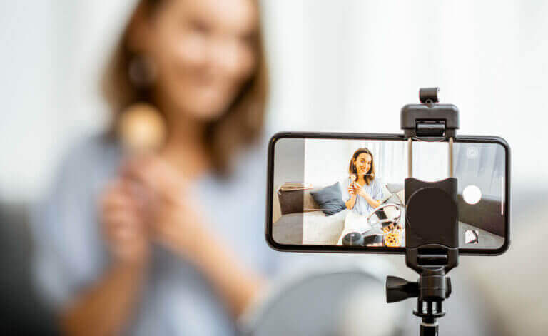 Young woman recording on a smart phone her vlog about cosmetics, showing and demonstrating makeup, close-up on phone. Influencer marketing in social media concept
