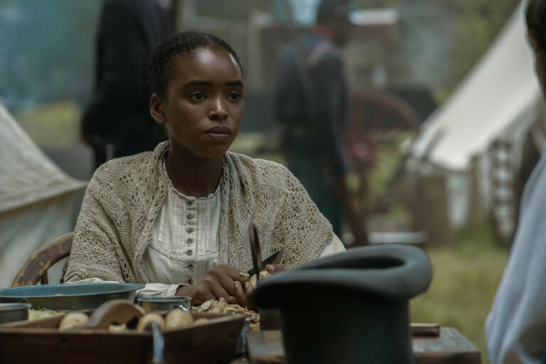 Lovie Simone in 1800s clothes sitting at table outside.