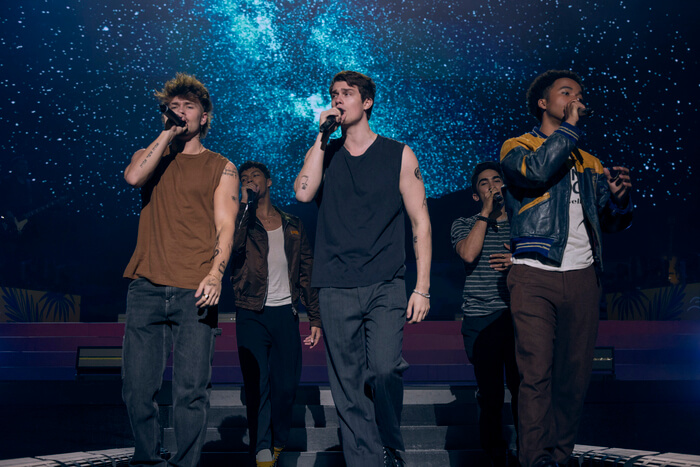 Nicholas Galitzine onstage singing with a boy band.