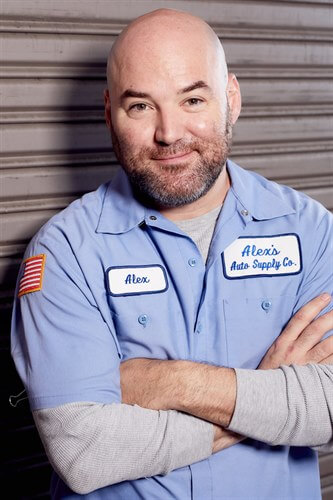 Orion McCabe in a mechanic uniform smiling in front of a gate.
