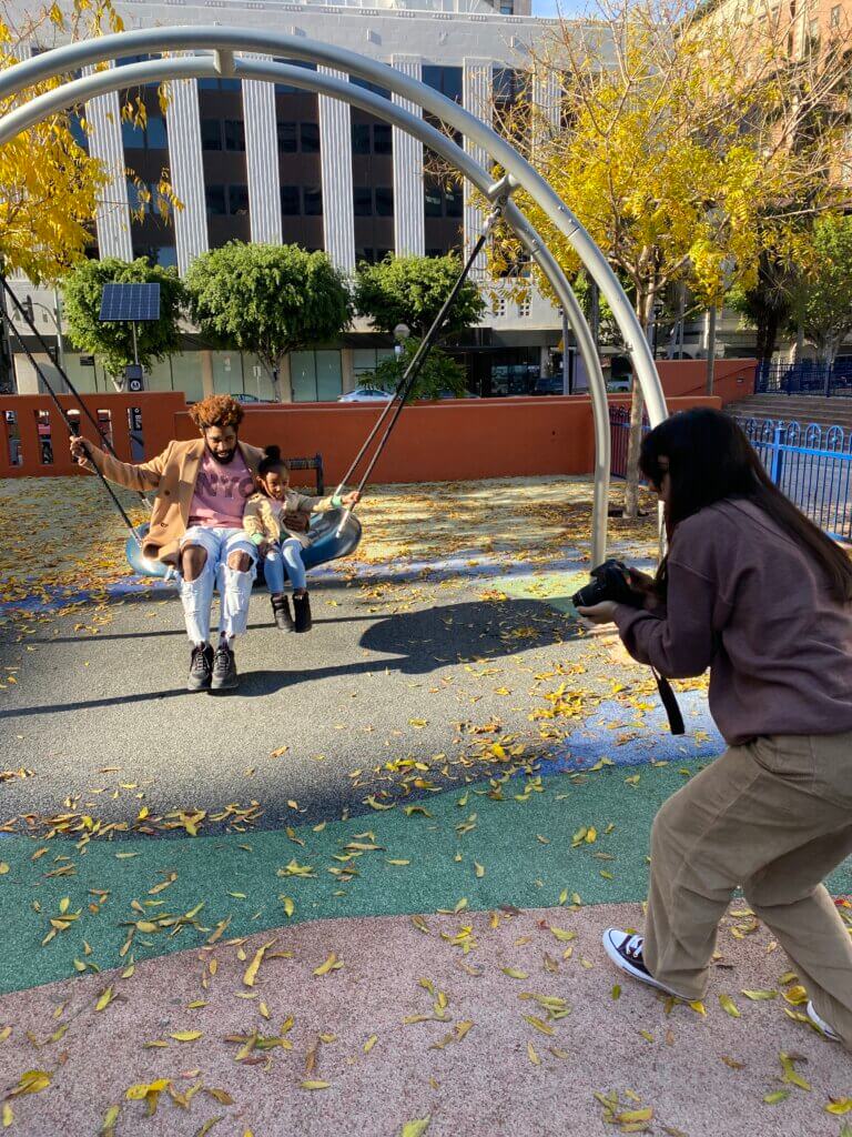 Photographer taking a picture of a man and child on a swing in the park.