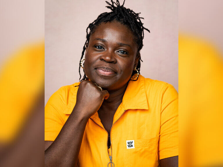 Aisha Bywaters smiling in a yellow shirt making a "thinker" pose.