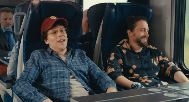 Jesse Eisenberg and Kieran Culkin laughing in a theater together in the movie A REAL PAIN.