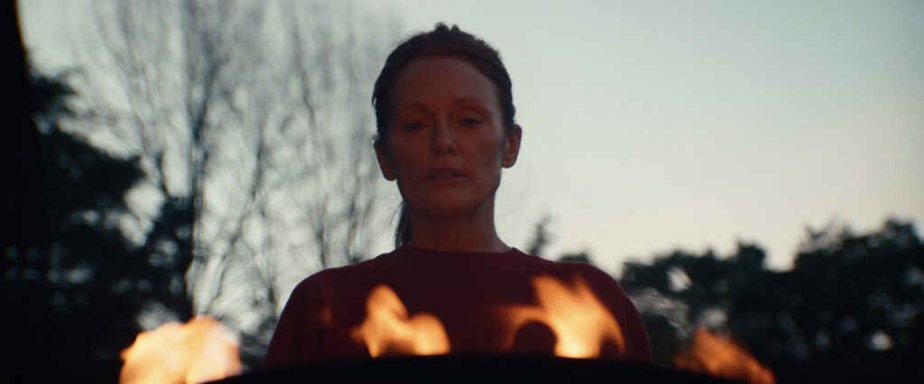 Julianne Moore standing outside over a fire in a red sweater looking concerned.